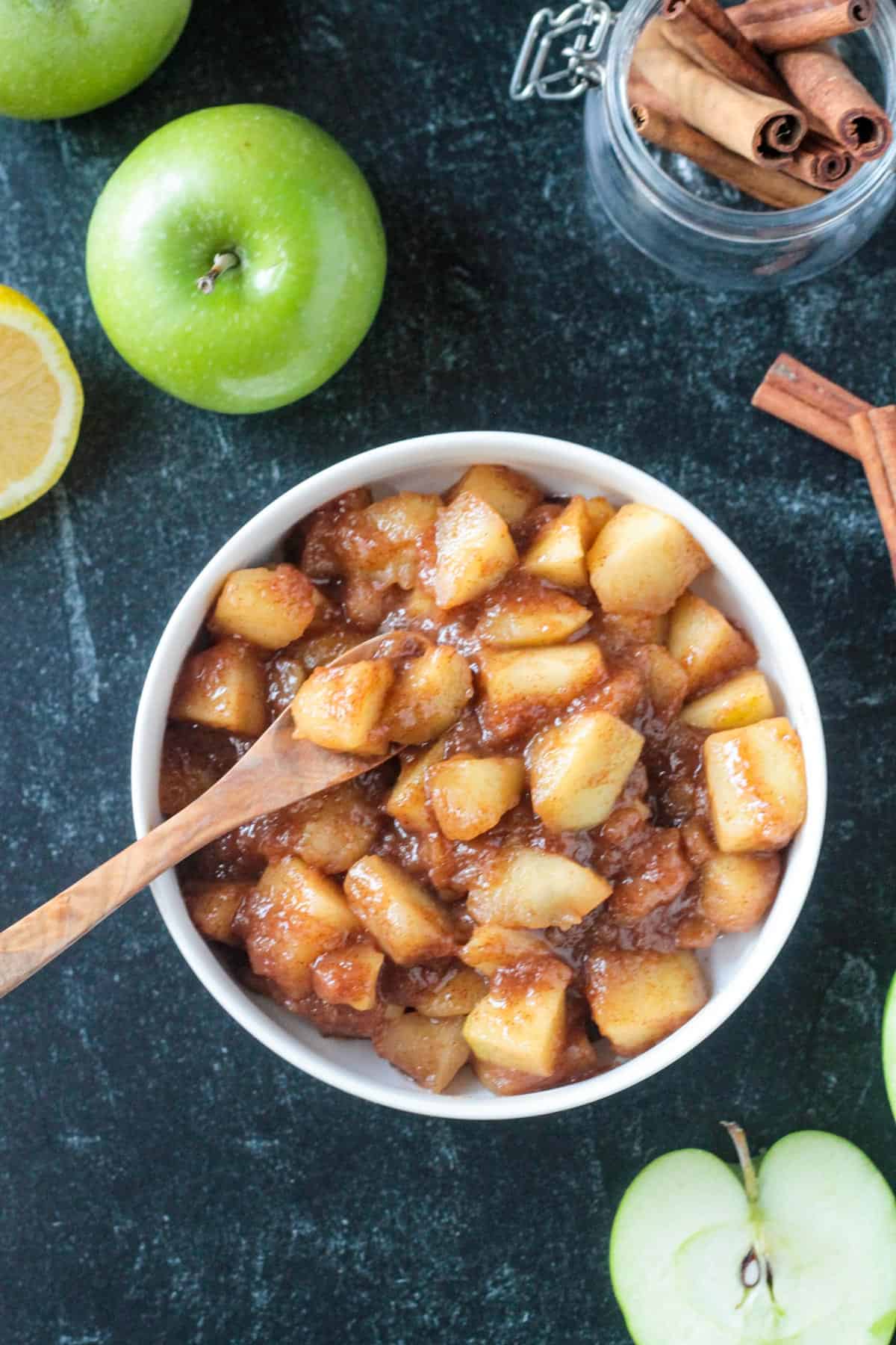 Small wooden spoon scooping up stovetop cinnamon apples from a bowl.