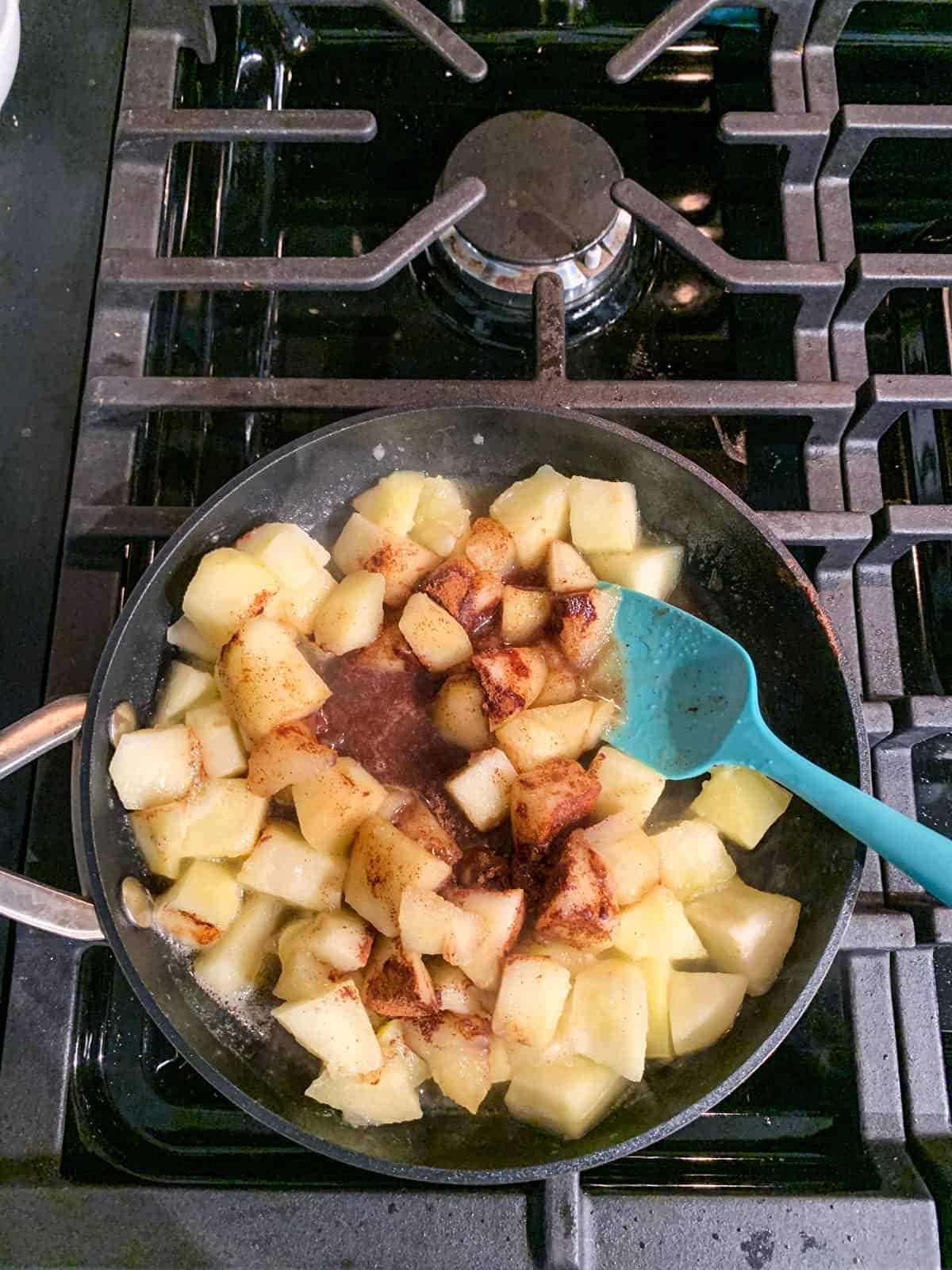 Cinnamon and maple syrup added to a skillet of diced fruit.