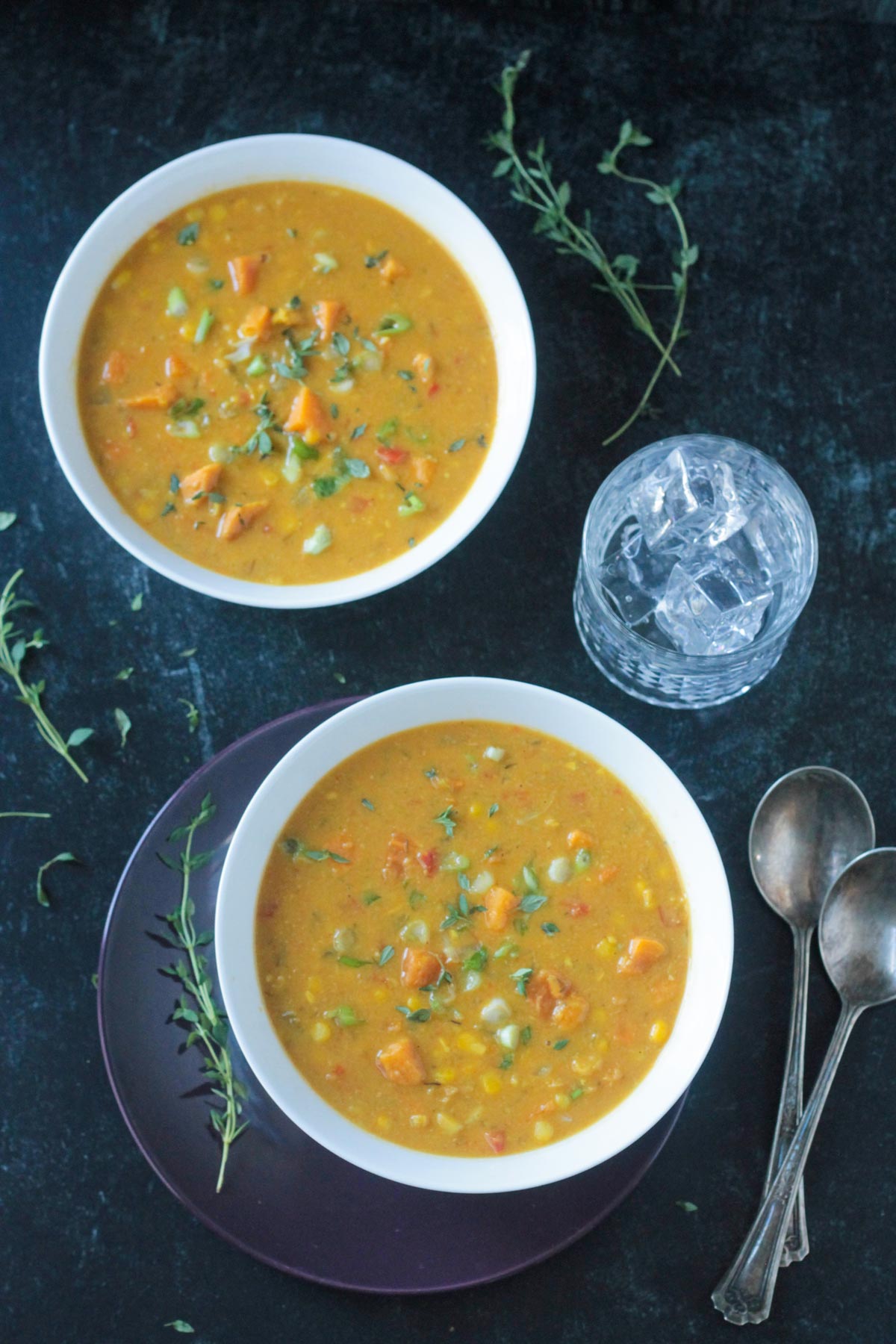 Two bowls of soup next to two spoons and a glass of water..