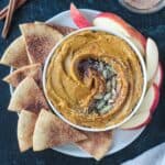 Sweet pumpkin hummus garnished with maple syrup and pumpkin seeds next to sweet pita chips.