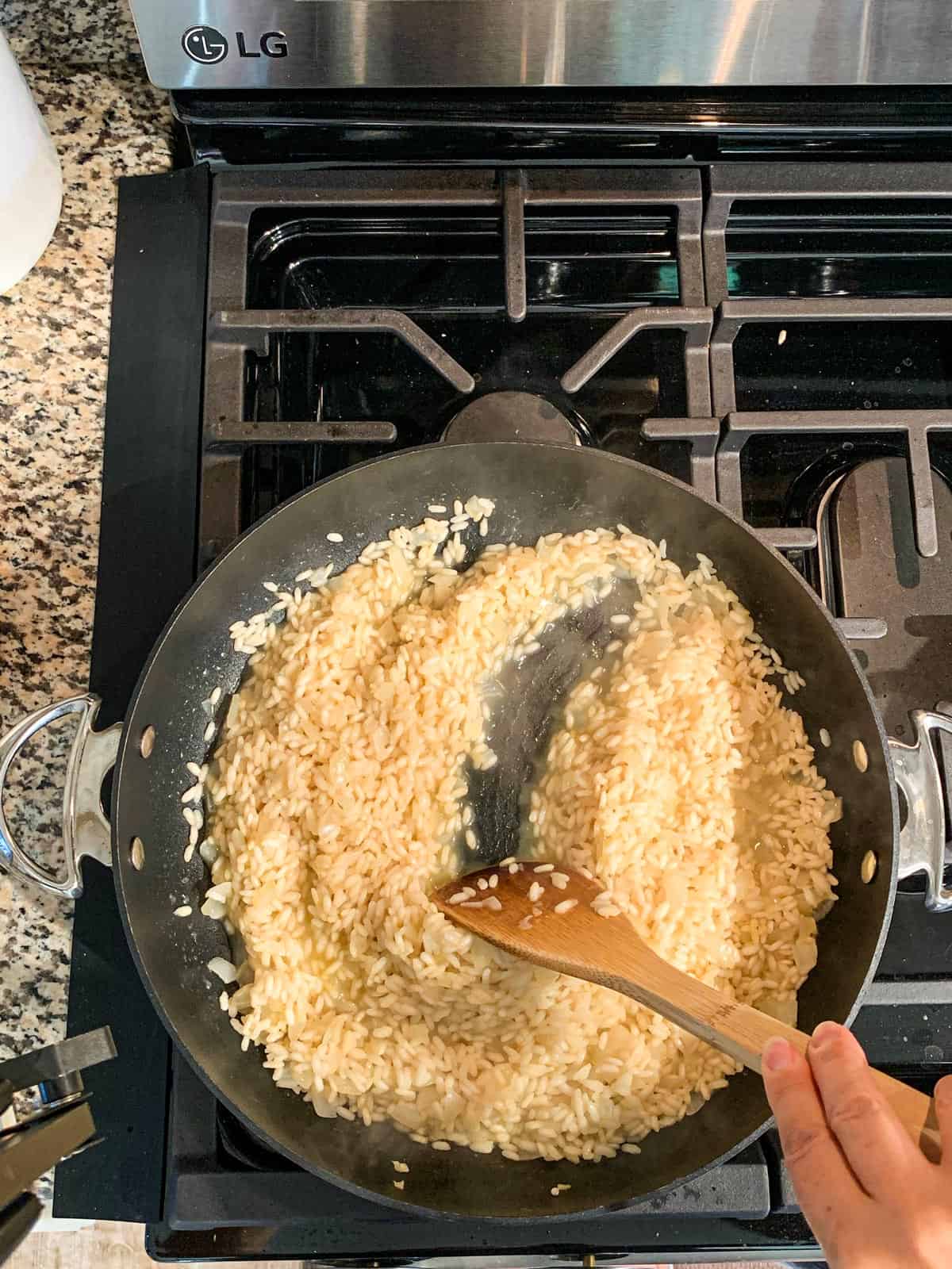 Wooden spoon streaking through a skillet of simmering arborio rice.