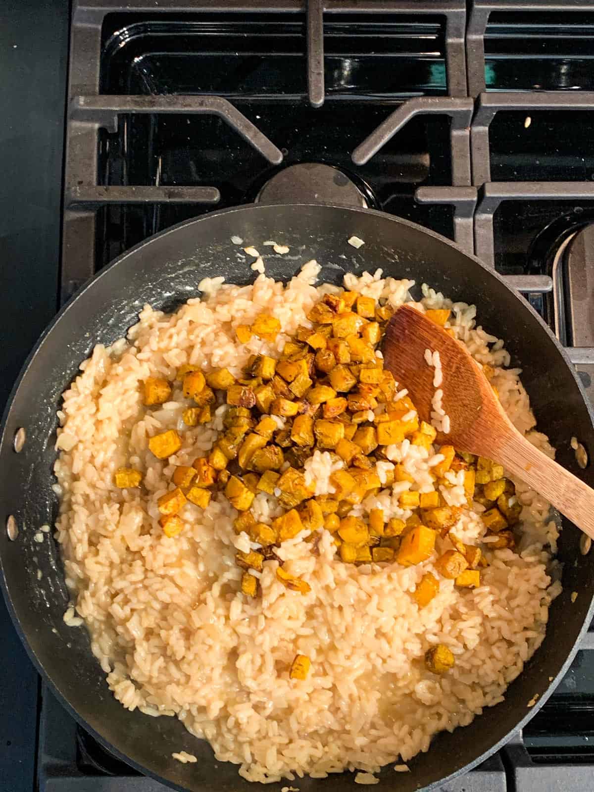 Adding roasted cubes of butternut squash into a pan of risotto.