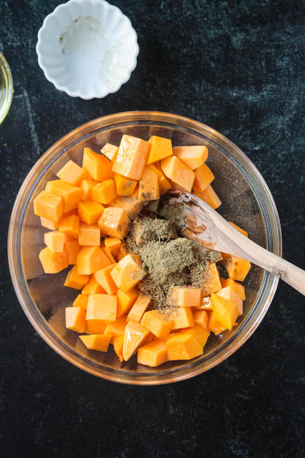 Diced raw butternut squash in a mixing bowl with spices.