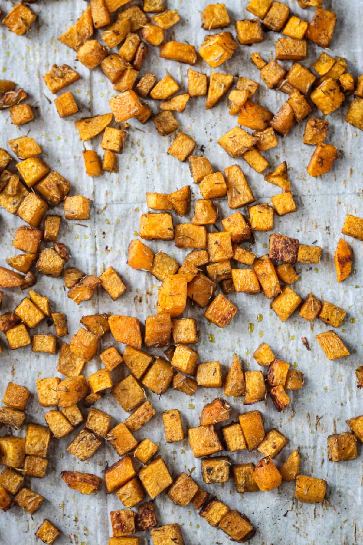 Roasted diced butternut squash on a parchment lined baking sheet.
