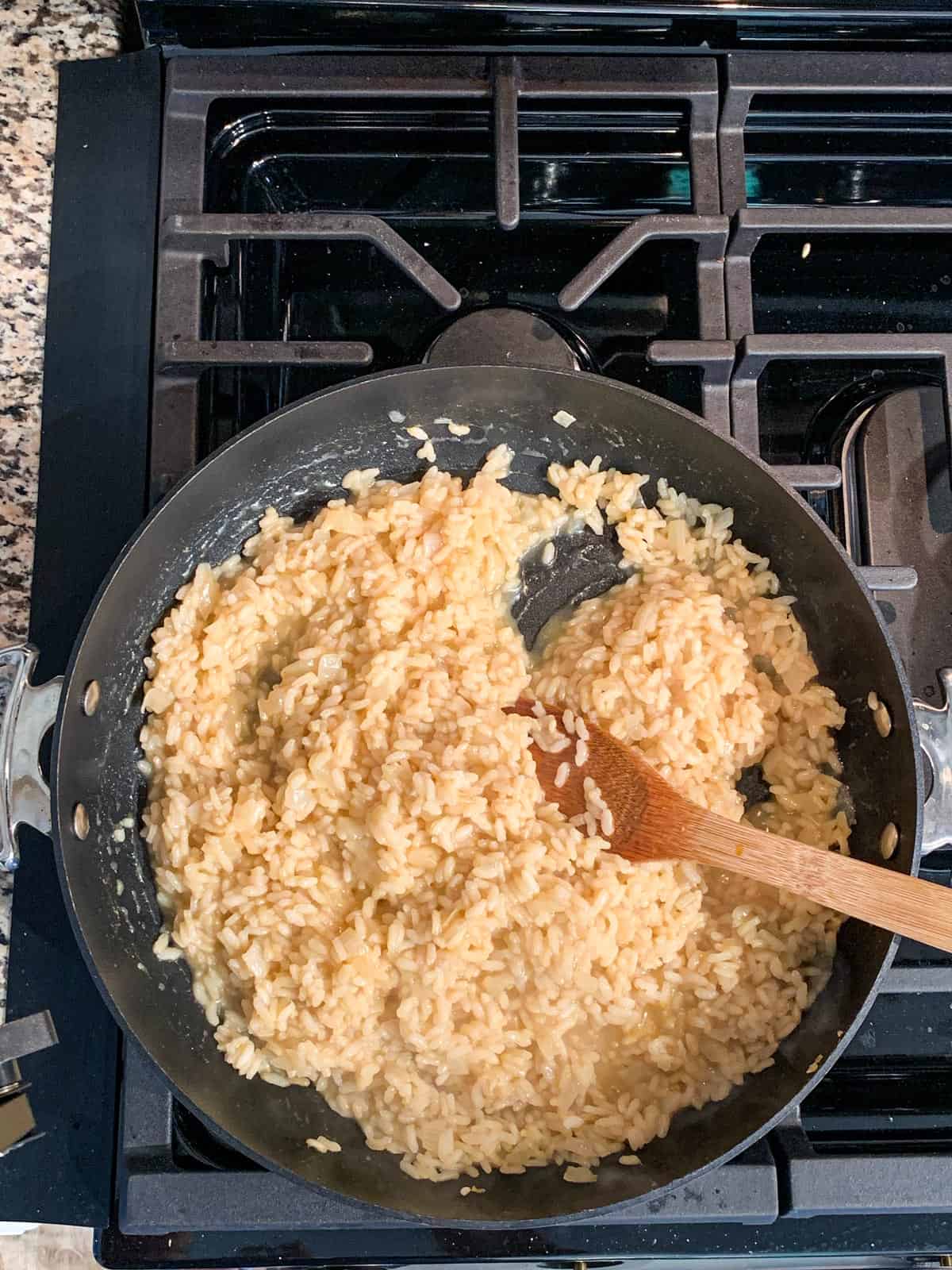 Wooden spoon stirring creamy risotto in a skillet.