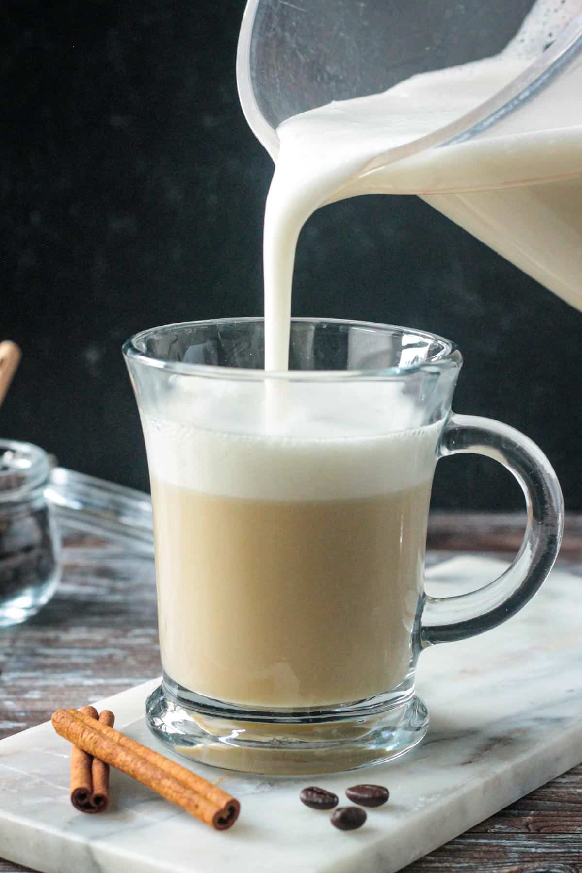 Pouring frothed milk on top of steamed milk and apple cider syrup in a glass.