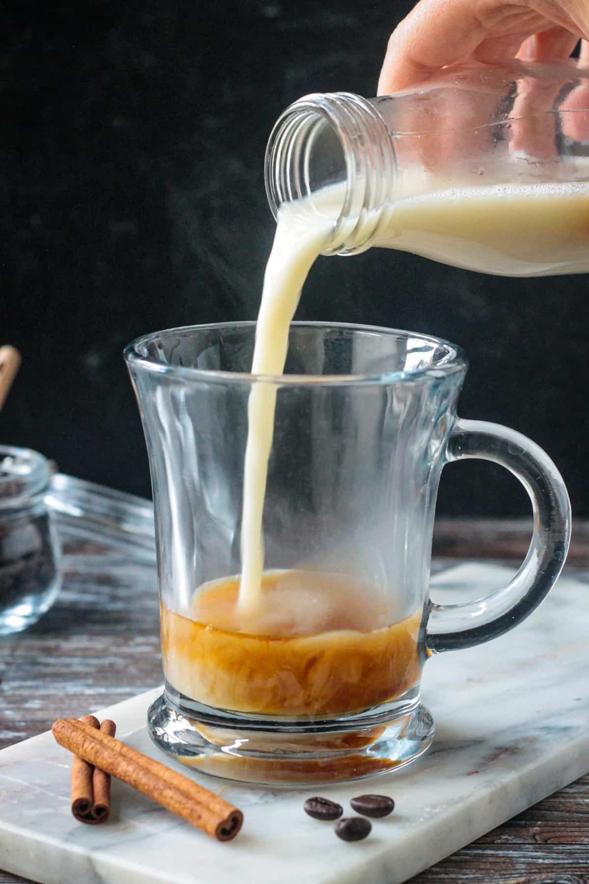 Pouring steamed milk over apple brown sugar syrup in a glass.