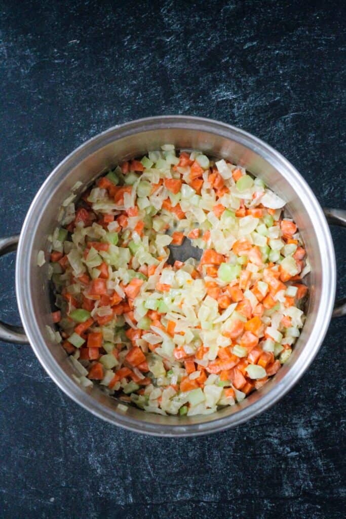 Sautéed diced onions, celery, and carrots in a soup pot.