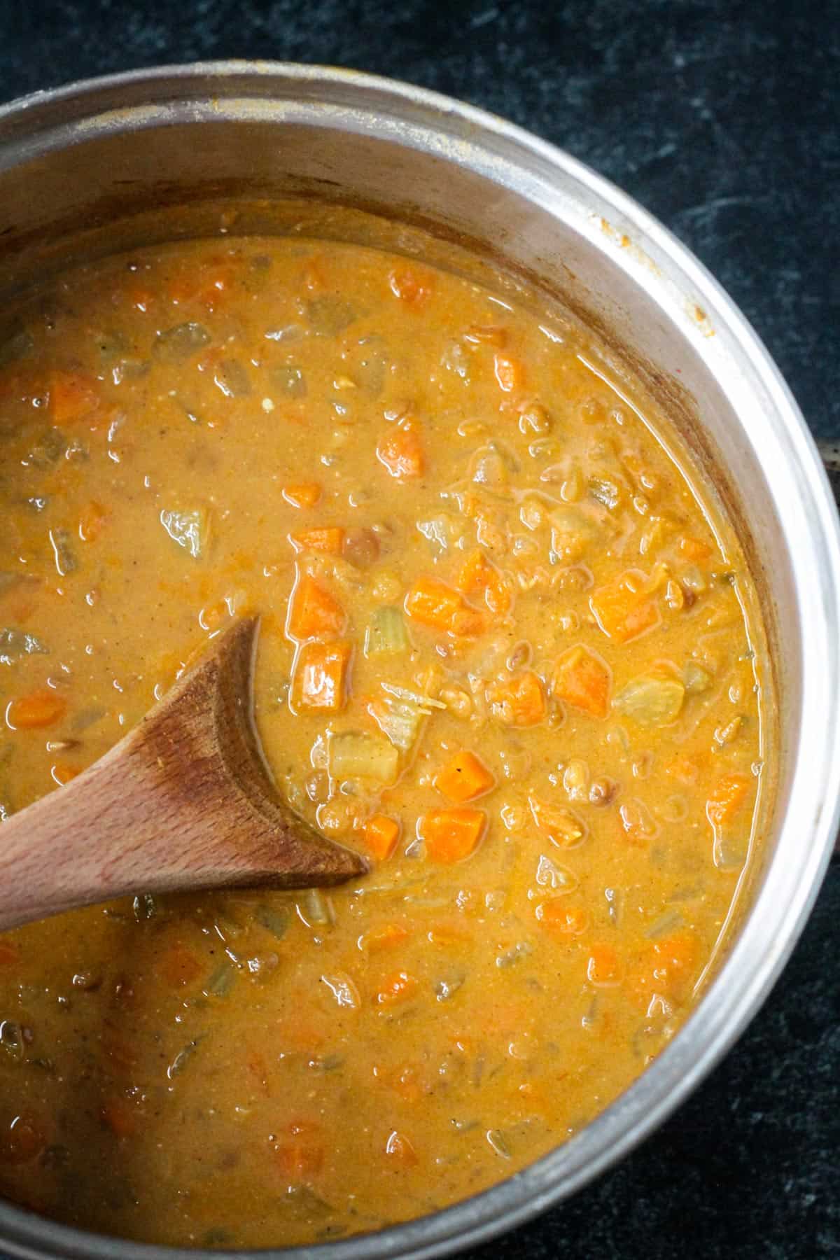 Close up of carrot lentil soup in a pot with a wooden spoon.