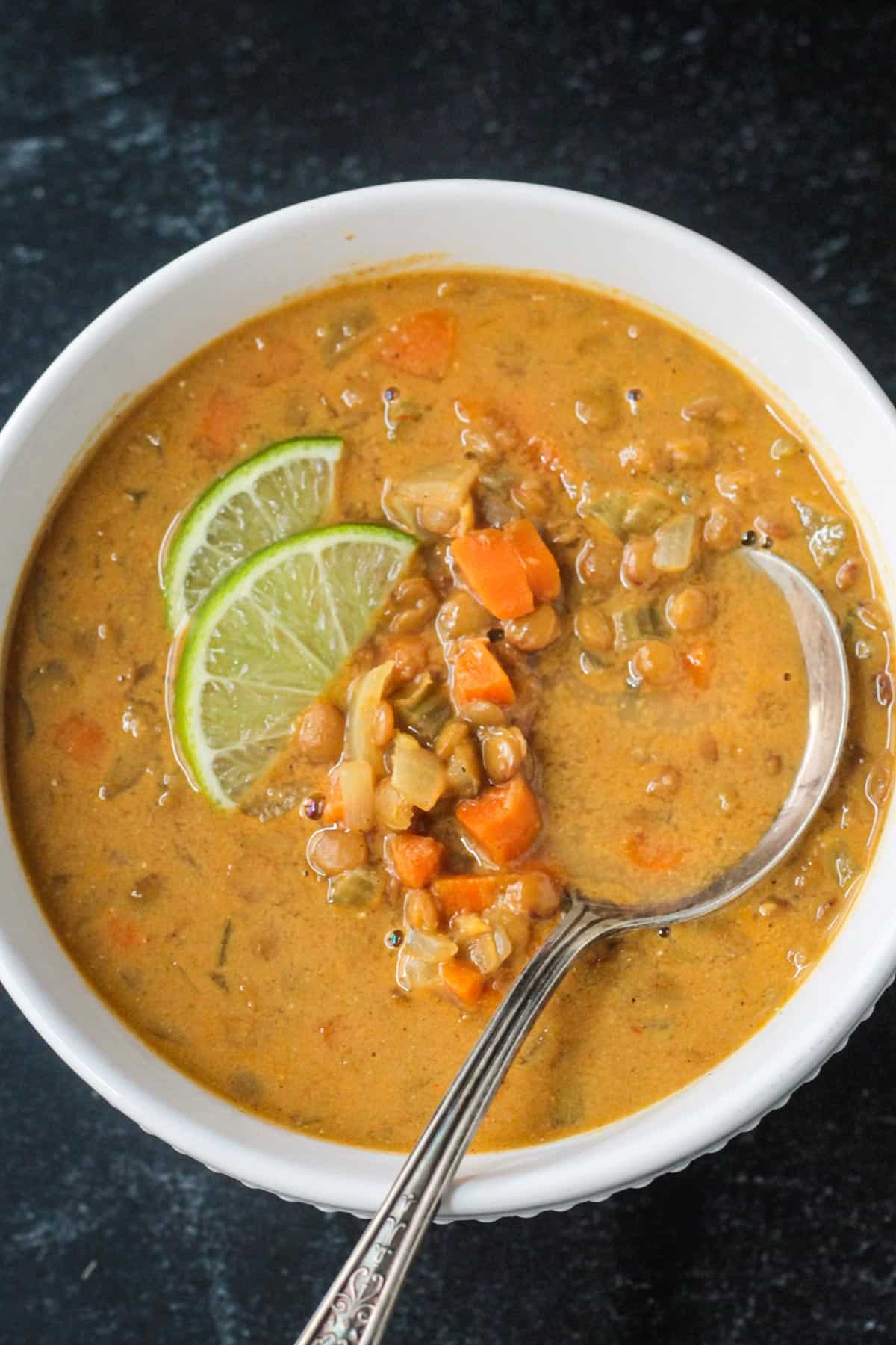 Metal spoon in a bowl of lentil soup garnished with two lime wedges.