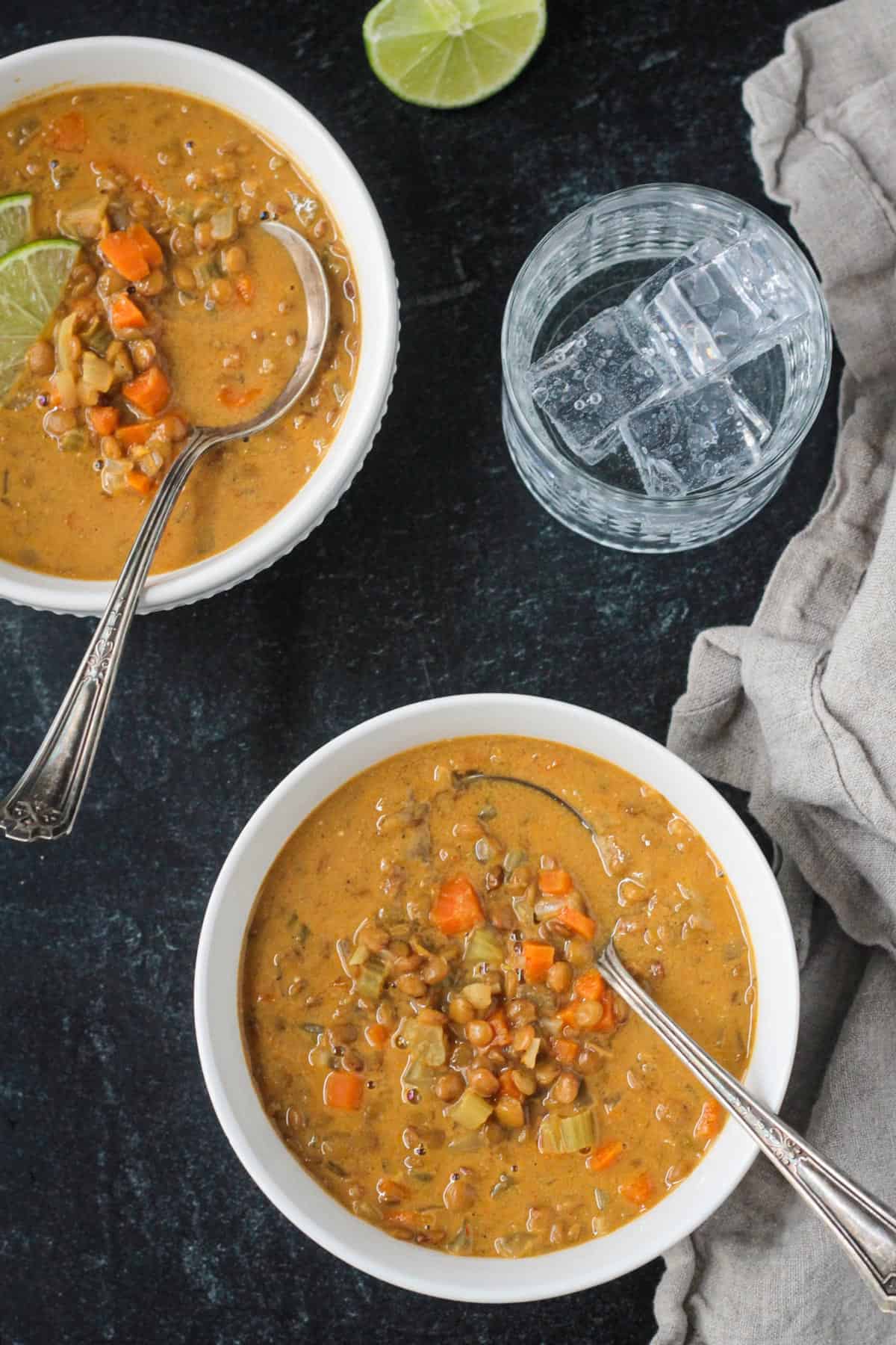 Two bowls of soup on table next to a glass of ice water.