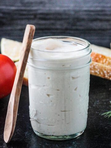 Small wooden spoon leaning against a jar of homemade vegan mayonnaise.