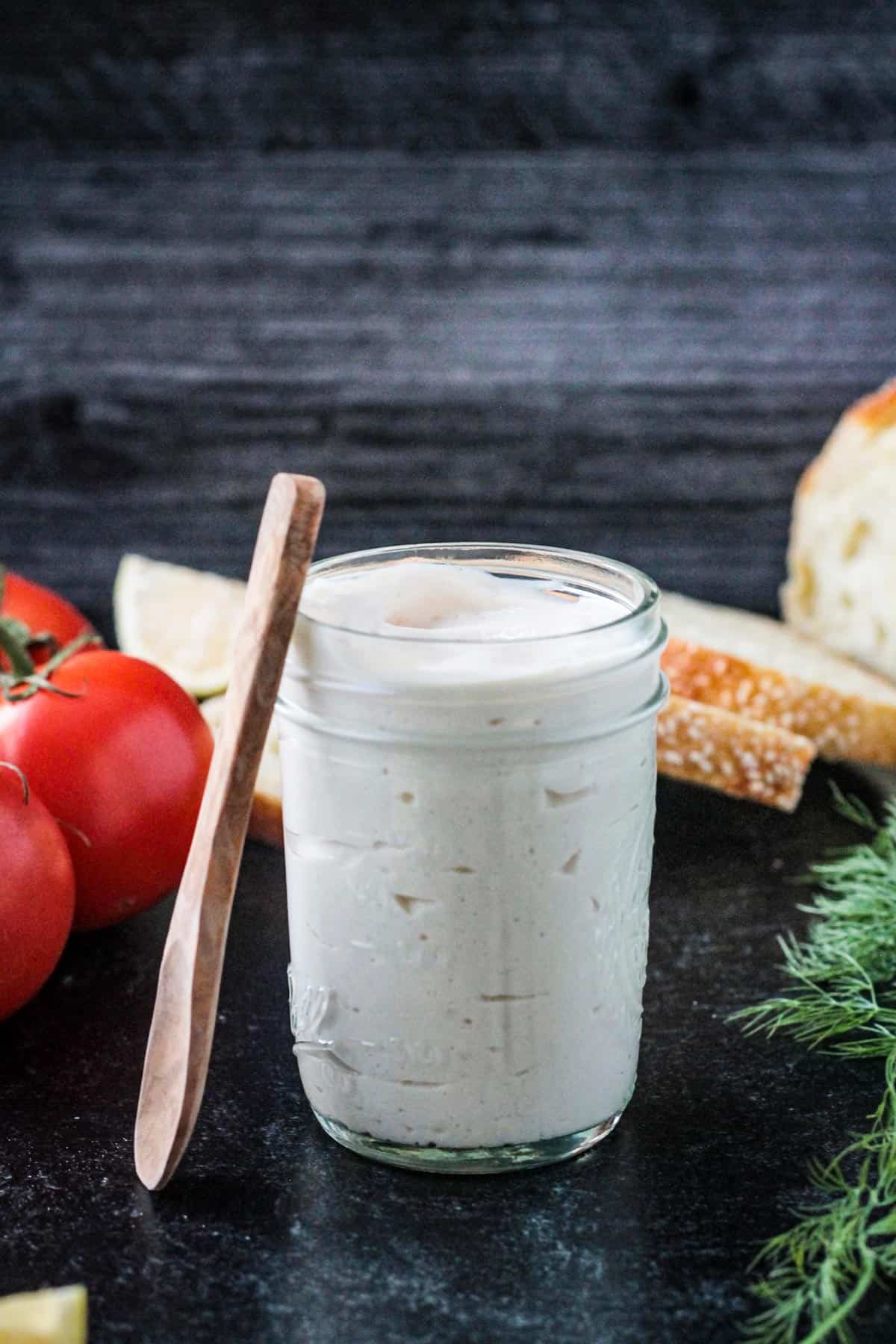 Small wooden spoon leaning against a jar of homemade vegan mayonnaise.