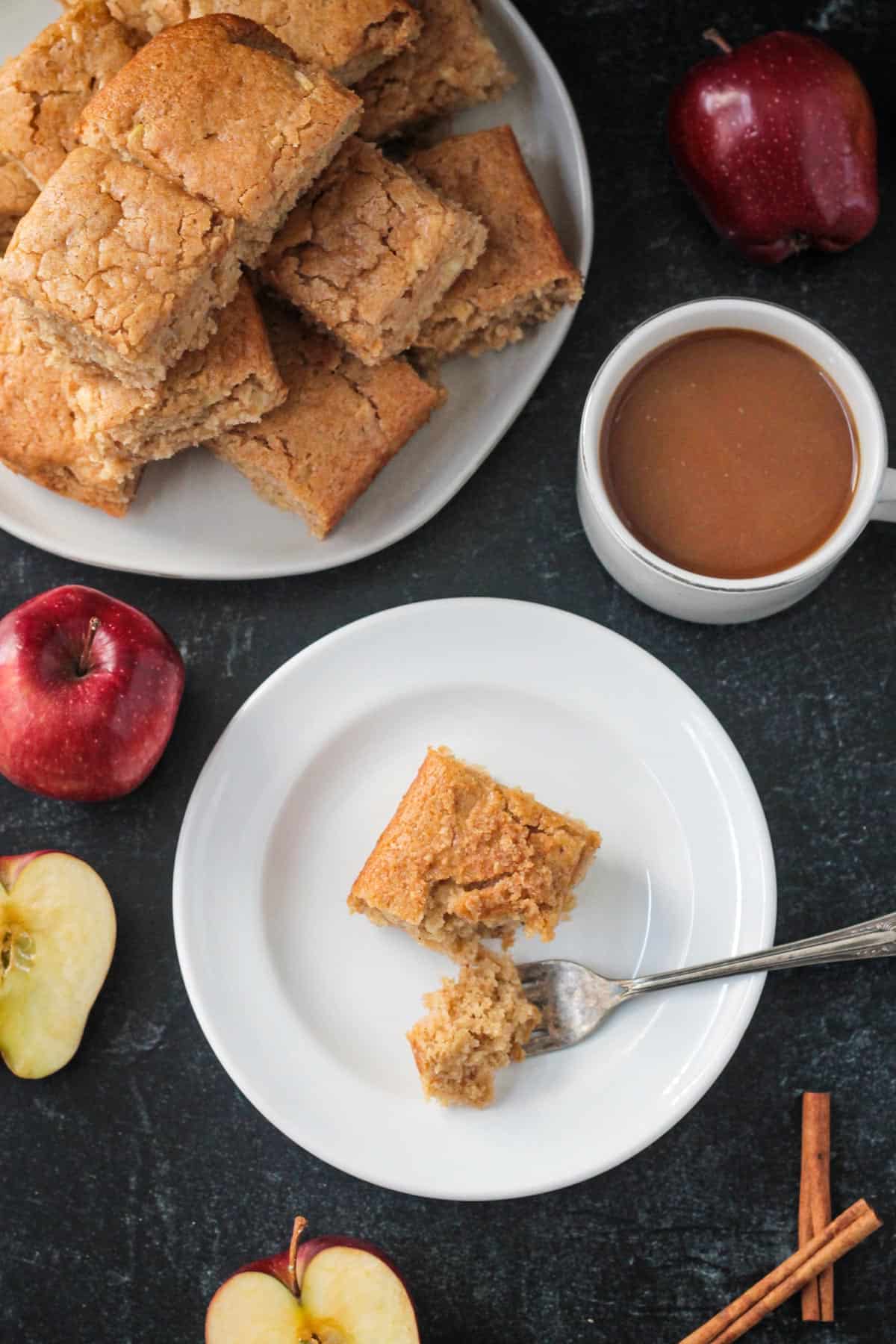 Slice of vegan apple cake with a bite on a fork on a white plate.