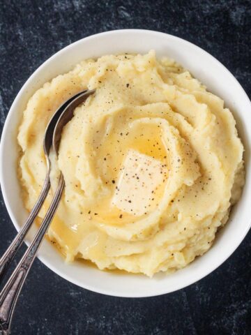Serving spoon in a bowl of creamy mashed potatoes topped with a pat of butter.
