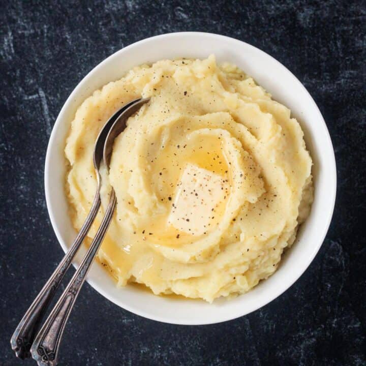 Serving spoon in a bowl of creamy mashed potatoes topped with a pat of butter.