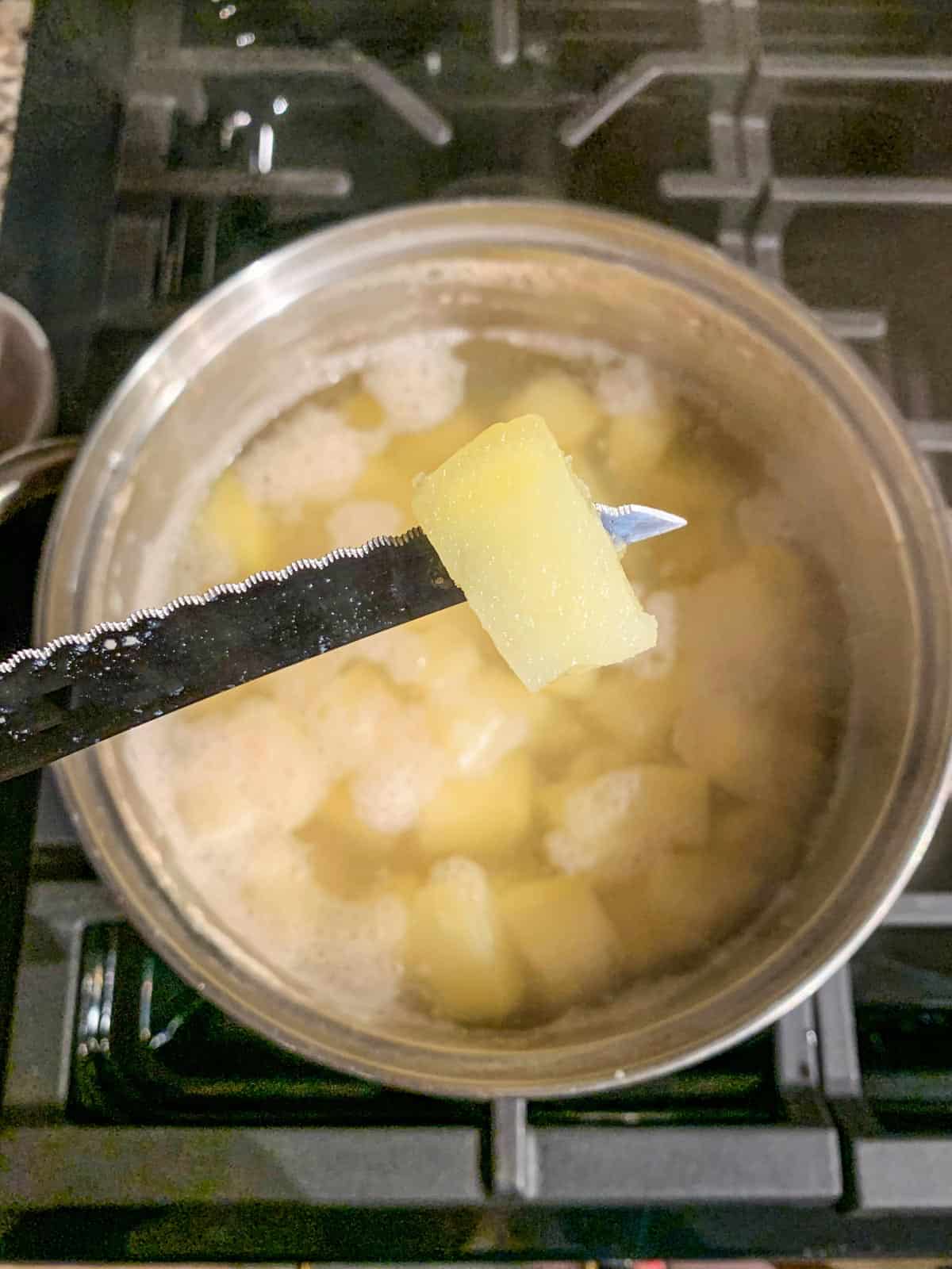 Knife through one diced potato in a pot.
