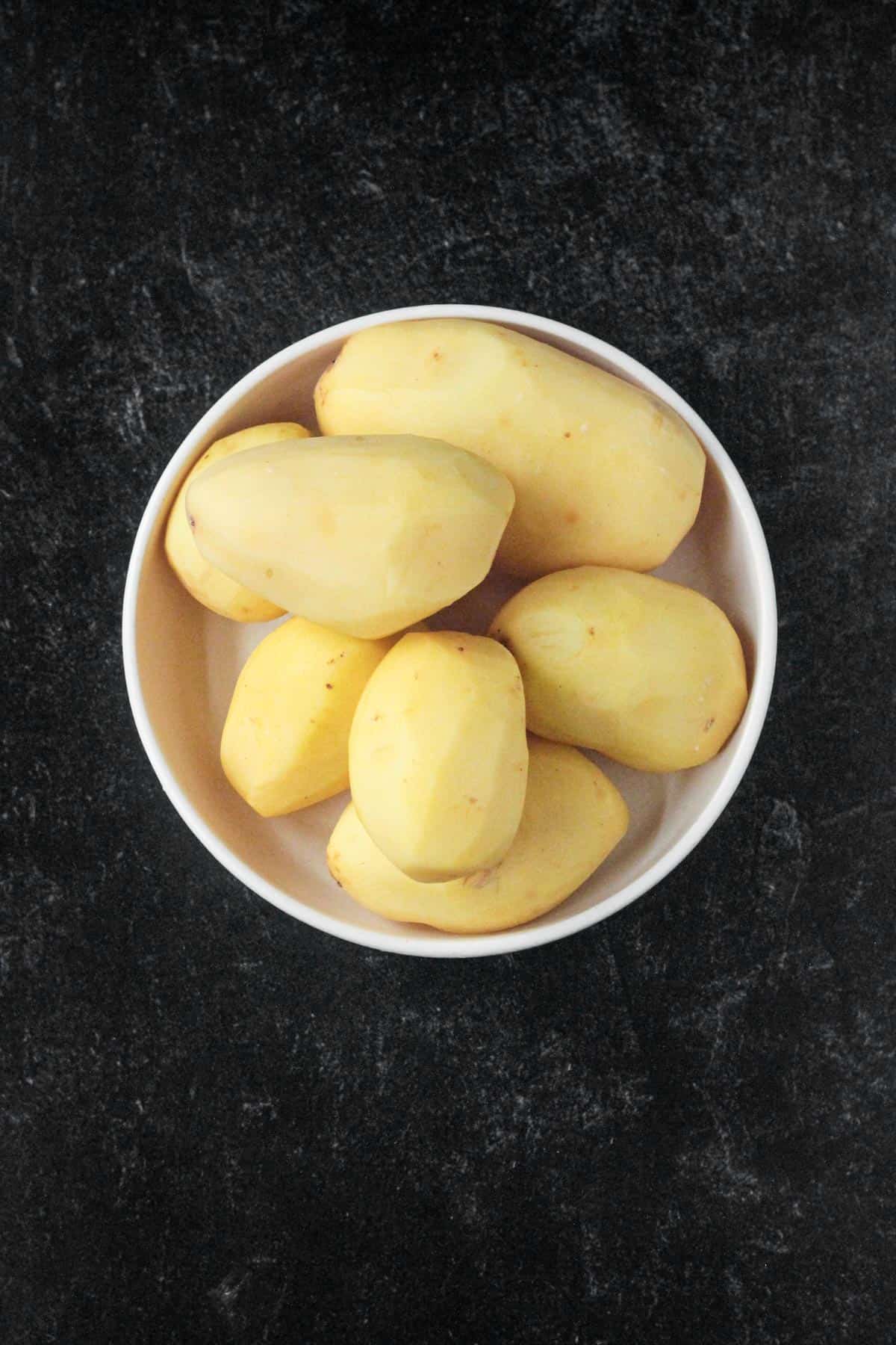 Peeled whole potatoes in a bowl.