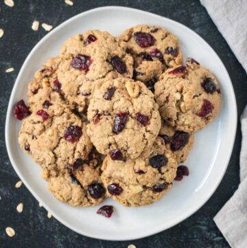 Pile of oatmeal cranberry walnut cookies on a plate.