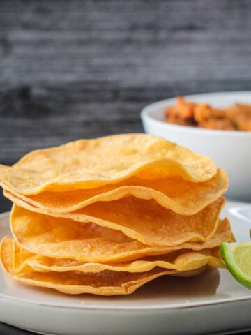 Stack of baked tostada shells with wavy edges.