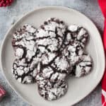 Pile of chocolate crinkle cookies dusted with powdered sugar on a plate.