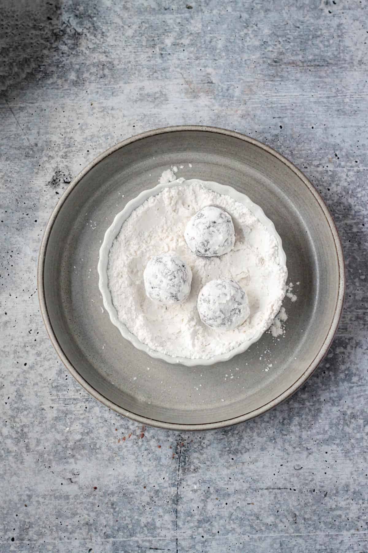 Three dough balls completely coated in powdered sugar.