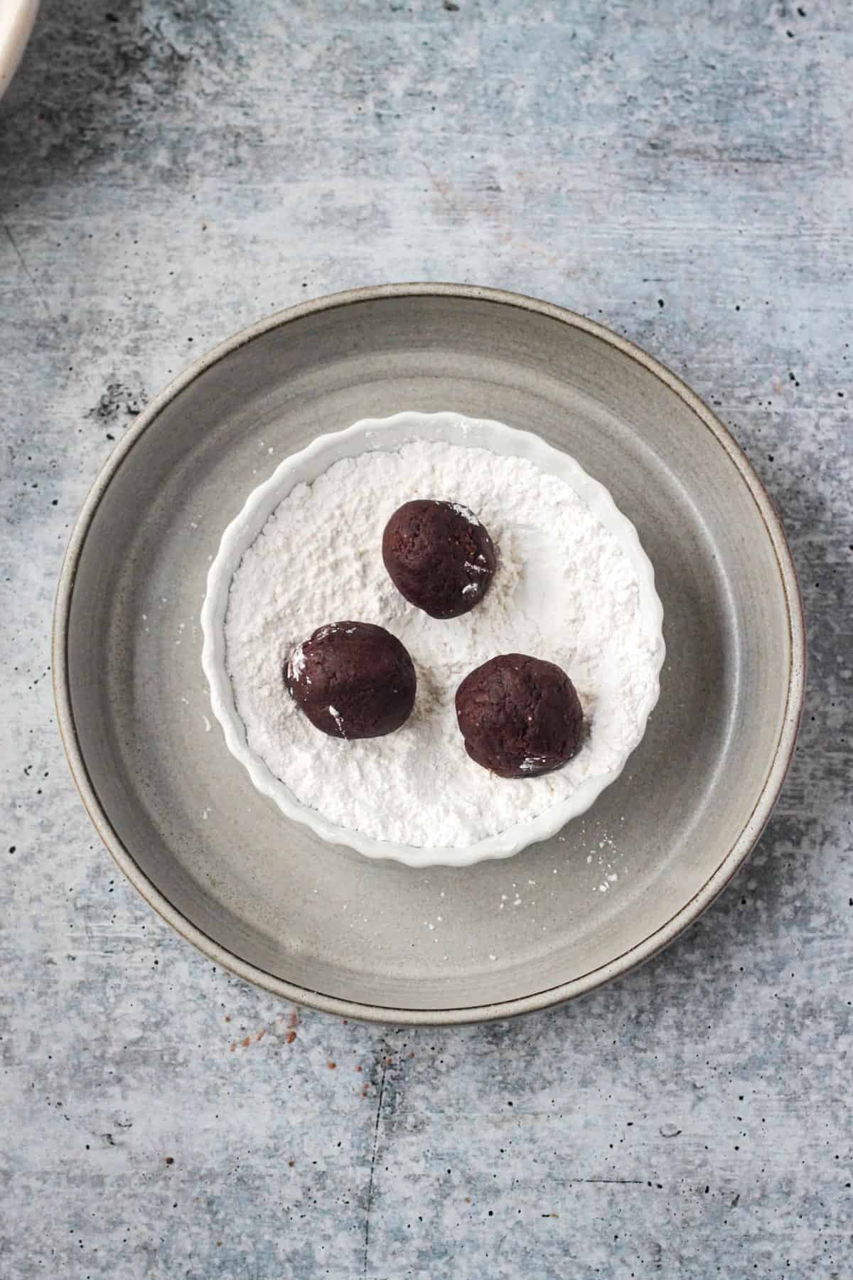 Three dough balls in a small bowl of powdered sugar.