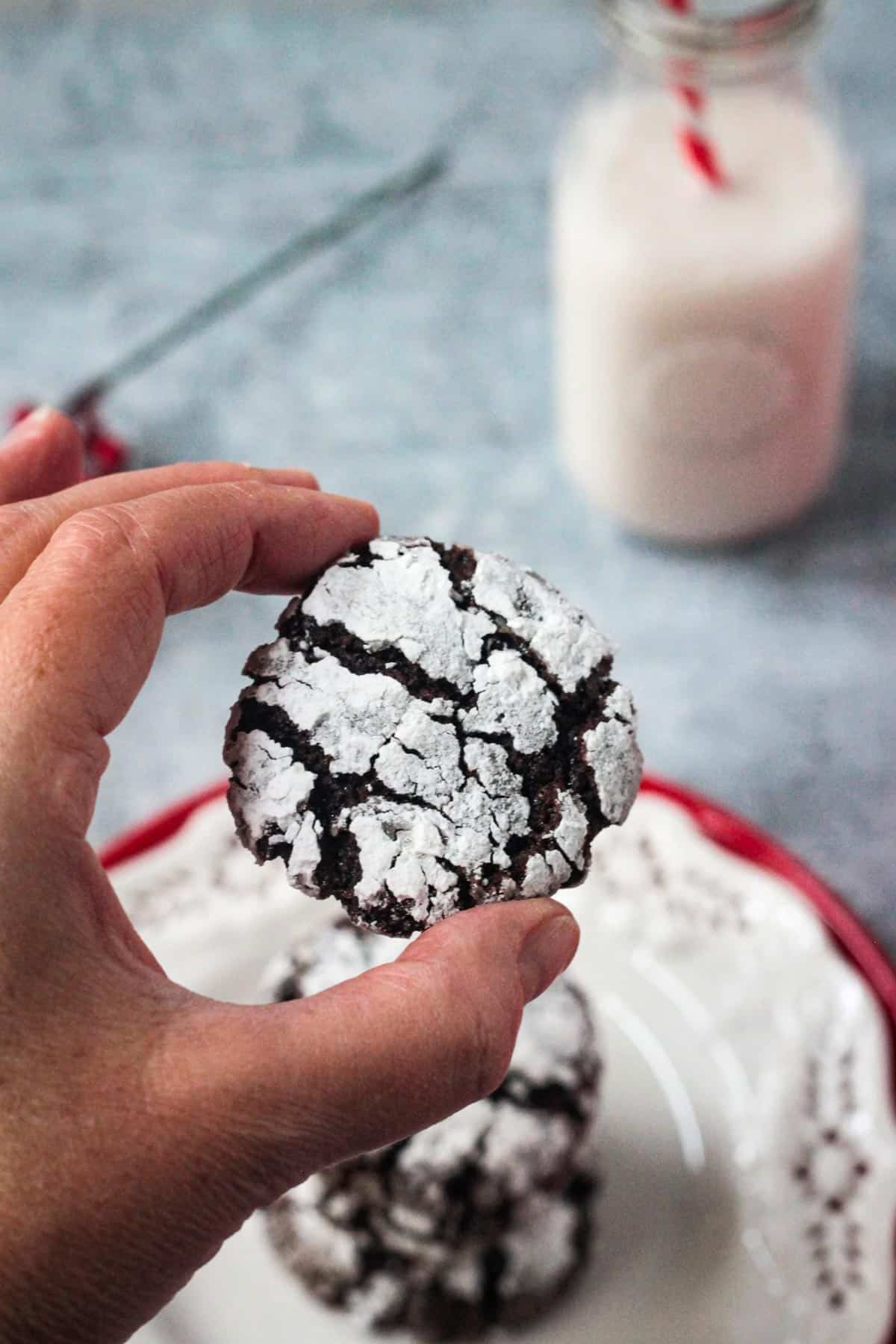 Hand holding up one cookie above a plate.