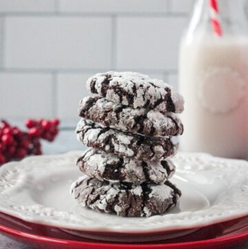 Stack of five chocolate crinkle cookies on a plate in front of a glass of milk.