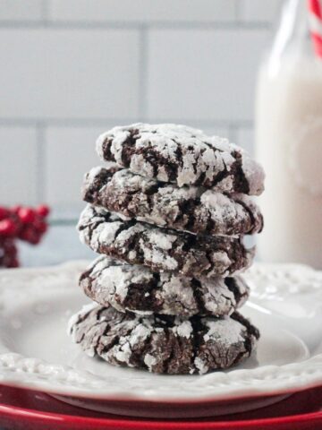 Stack of five chocolate crinkle cookies on a plate in front of a glass of milk.