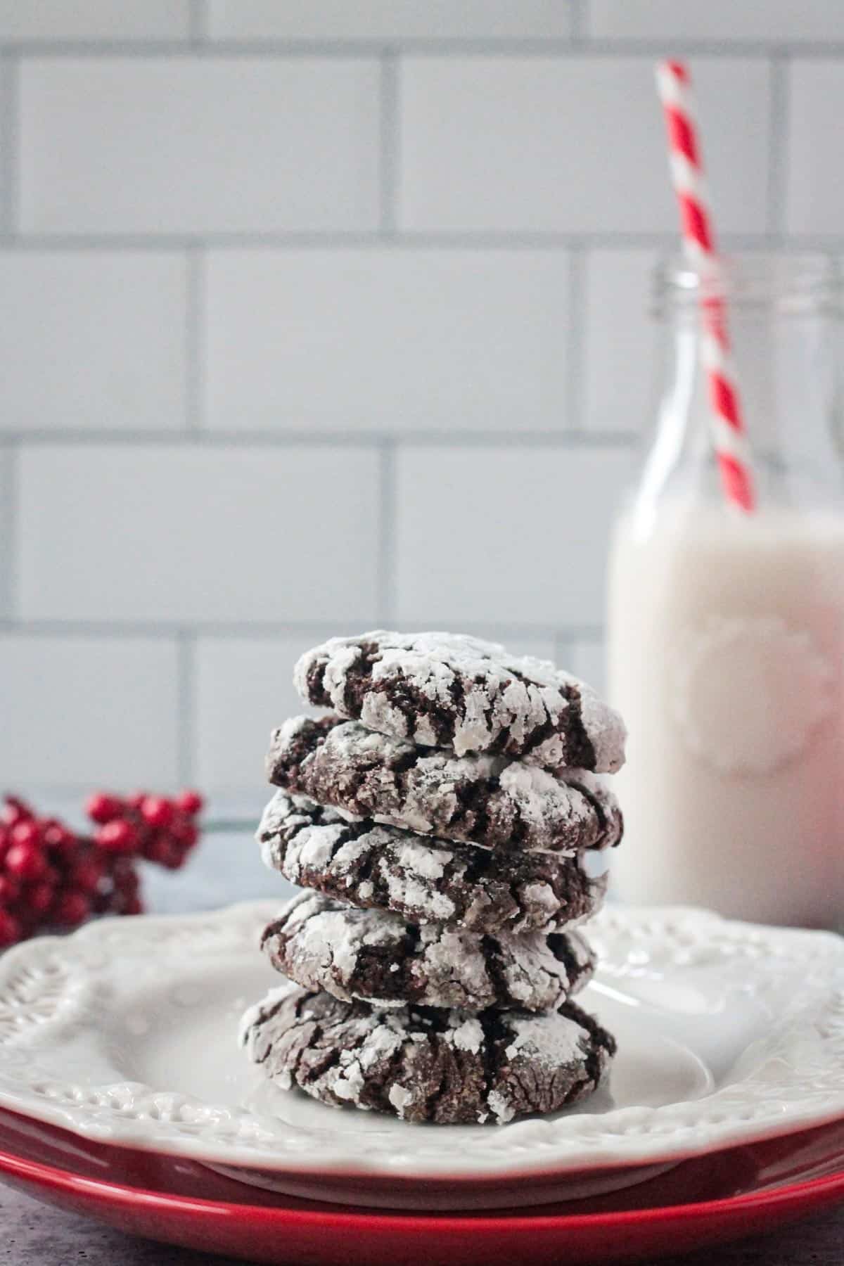 Stack of five chocolate crinkle cookies on a plate in front of a glass of milk.