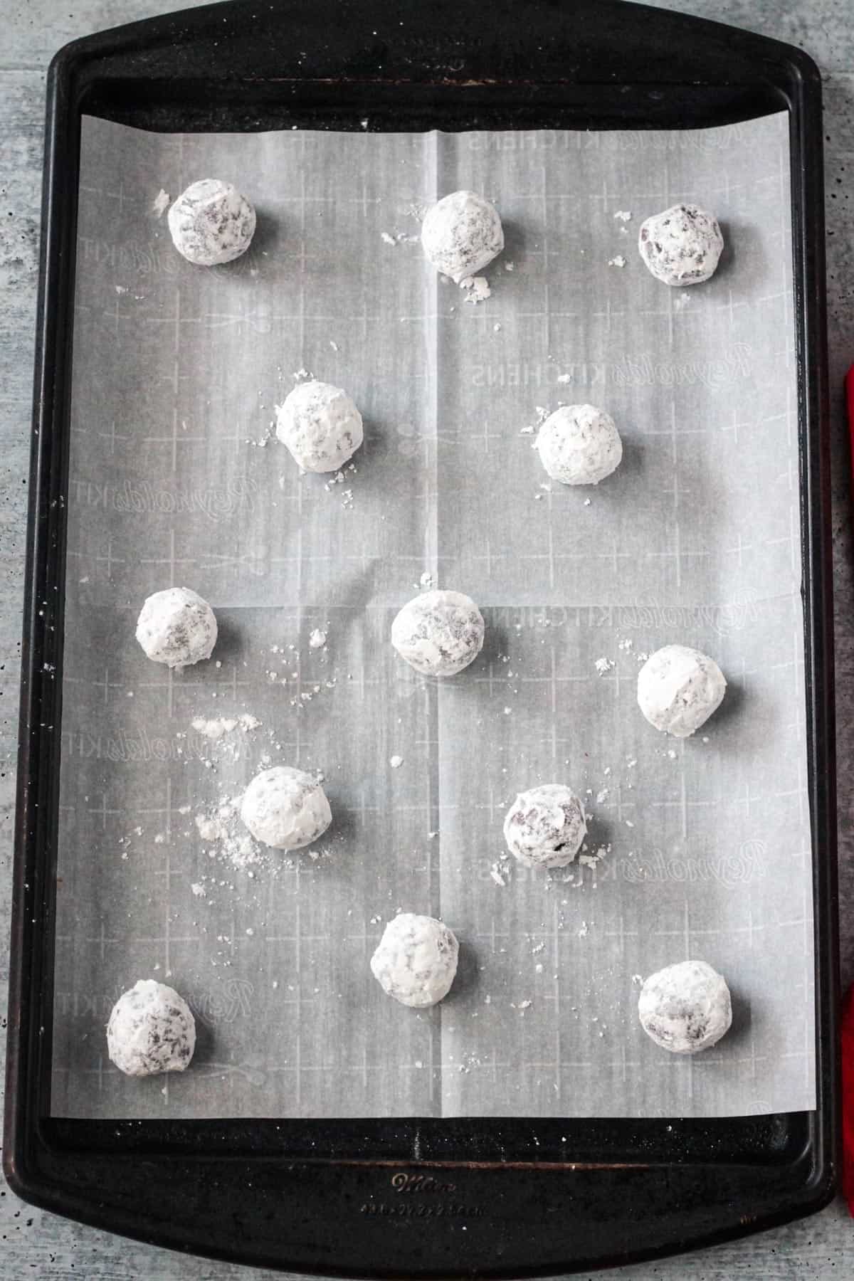 Dough balls coated in powdered sugar spaced out on a cookie sheet.