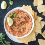 Bowl of vegan refried beans garnished with a lime wedge and surrounded by tortilla chips.