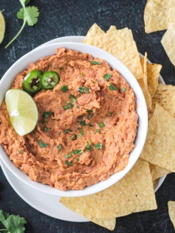 Bowl of vegan refried beans garnished with a lime wedge and surrounded by tortilla chips.