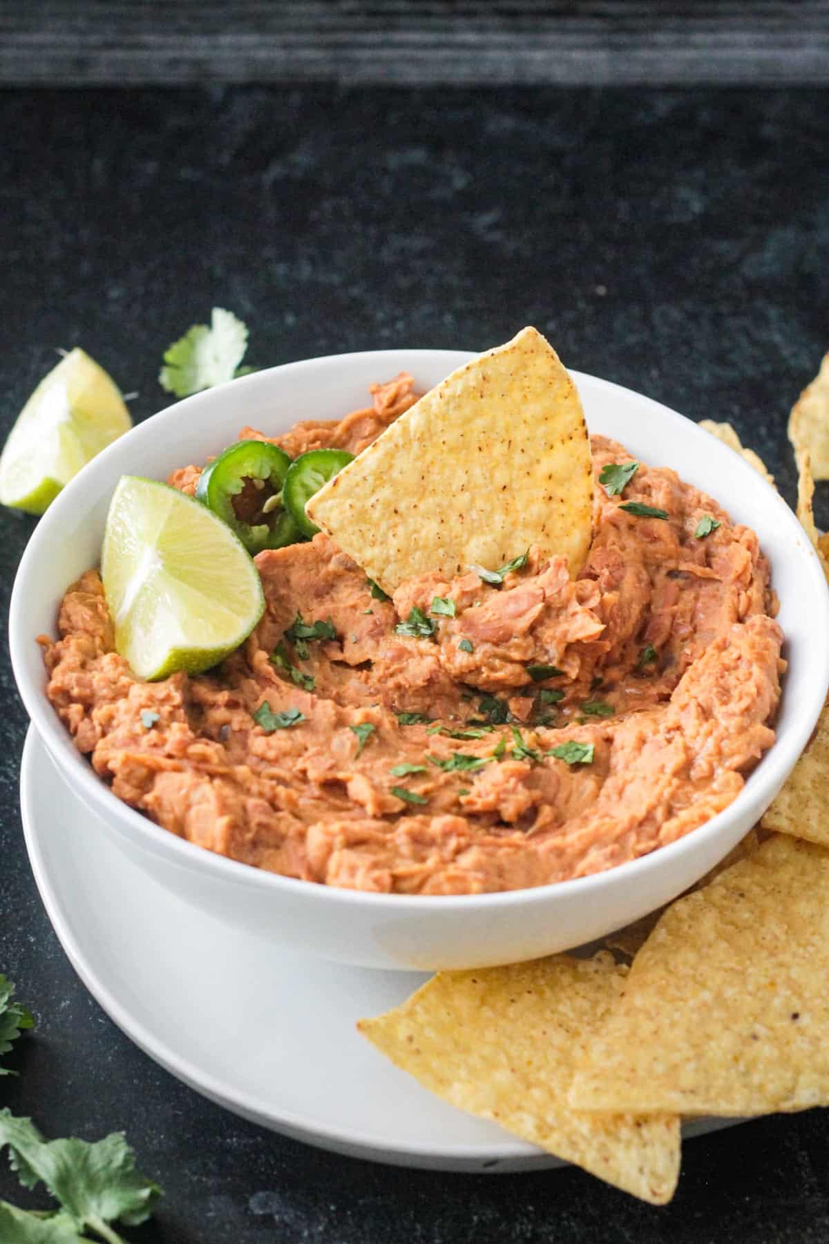 Tortilla chip standing up in a bowl of creamy pinto beans.