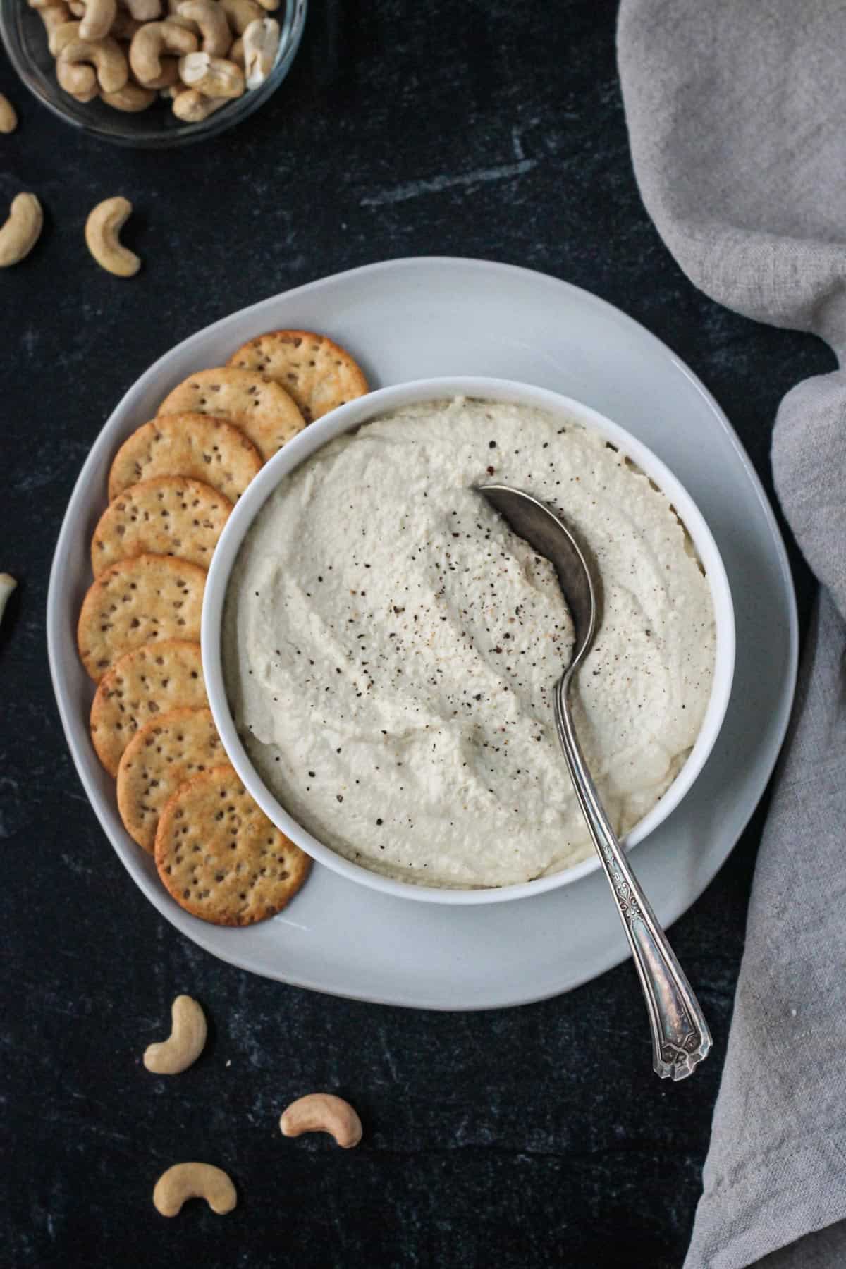 Vegan ricotta in a serving bowl on a plate with crackers.