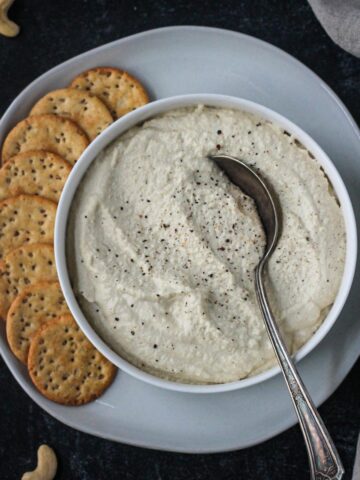 Vegan ricotta in a serving bowl on a plate with crackers.