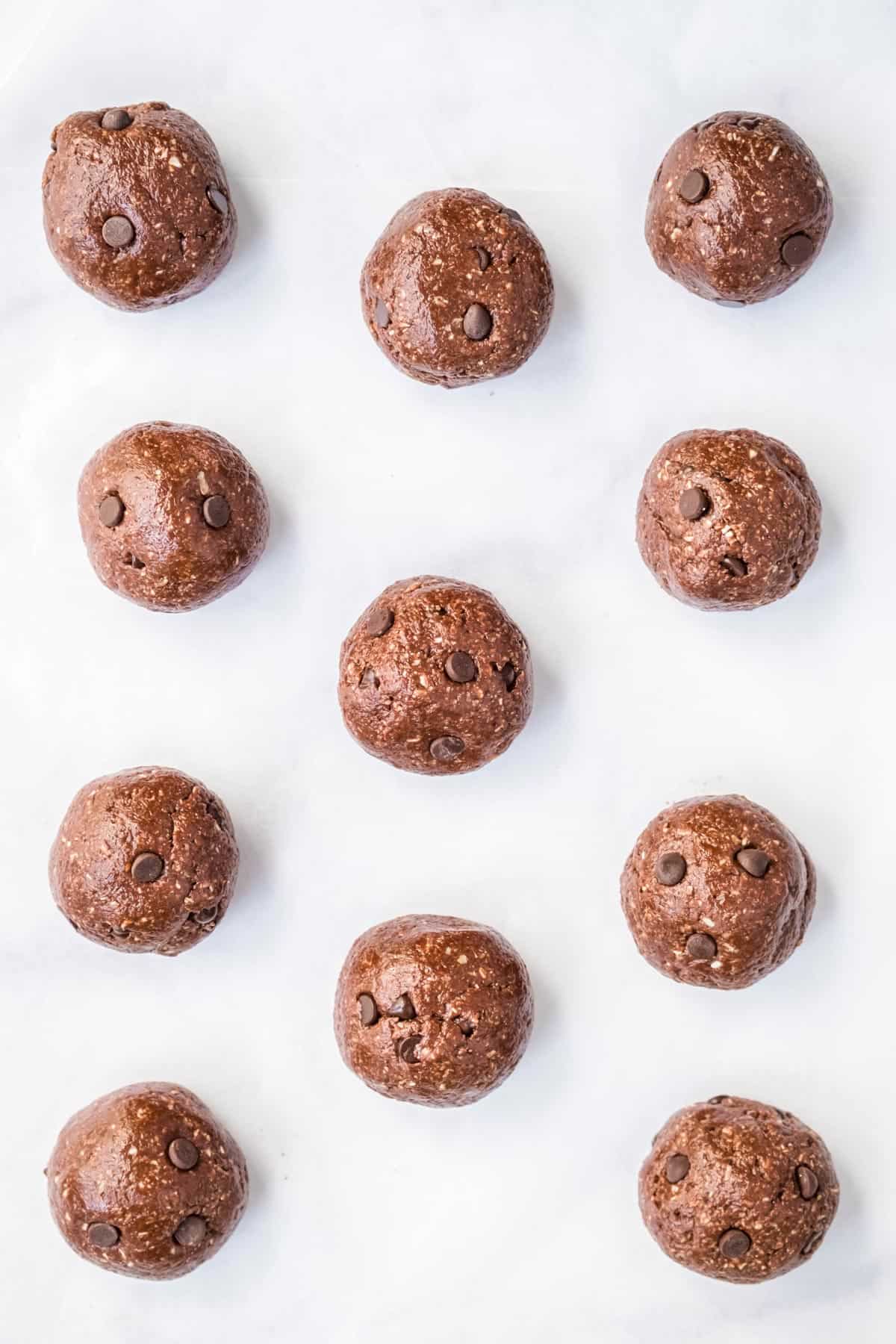 Eleven edible brownie batter dough balls spaced out on a parchment lined cookie sheet.