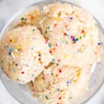 Overhead view of cookie dough in a glass next to a bowl of sprinkles.
