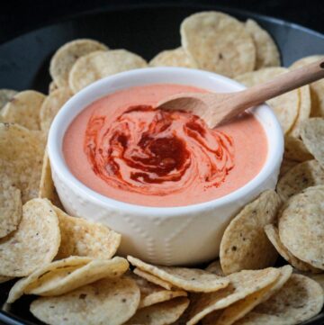 Harissa yogurt sauce in a white bowl surrounded by round tortilla chips.