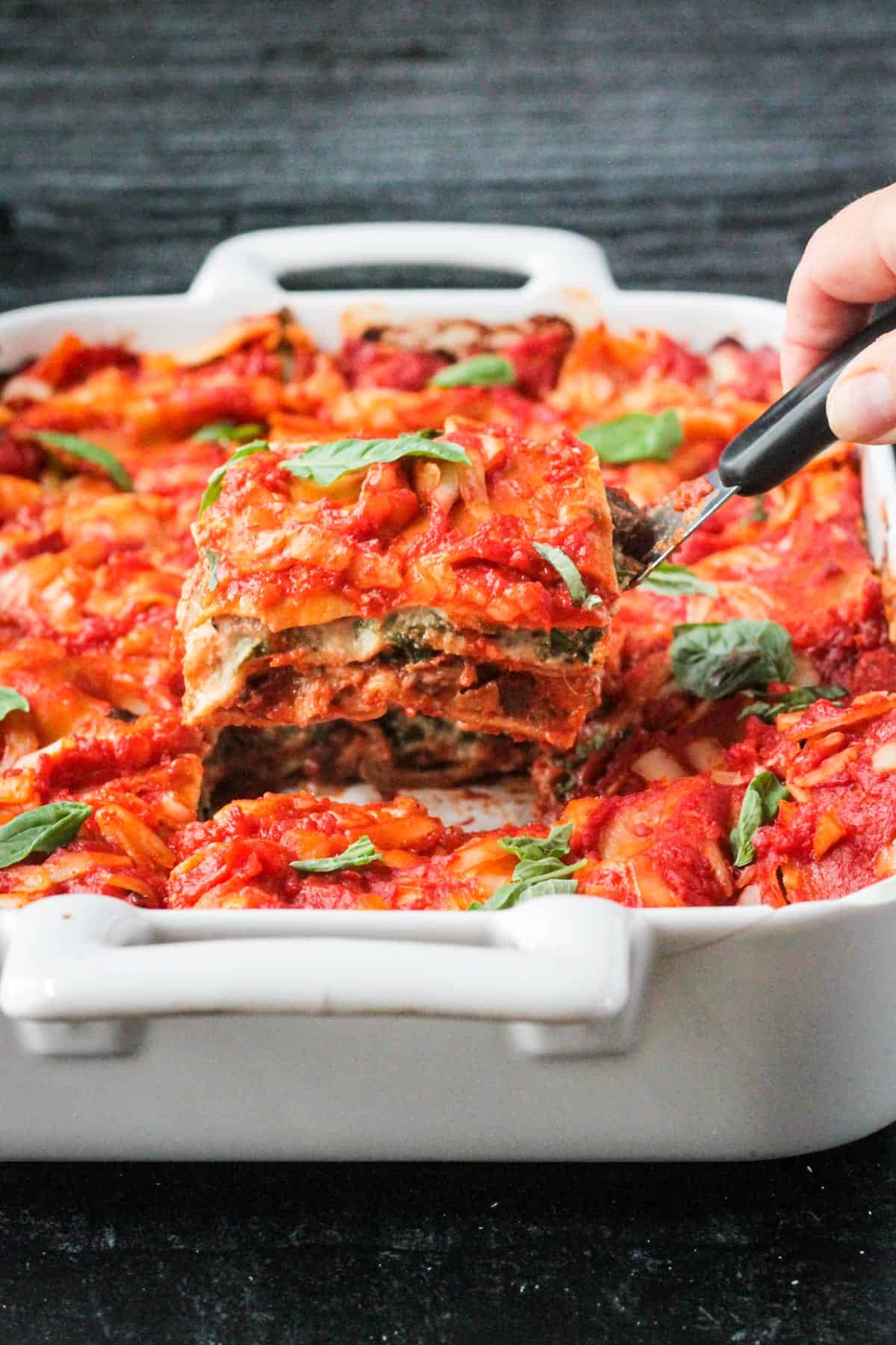 A slice of vegetable lasagna on a spatula being lifted out of the baking dish.
