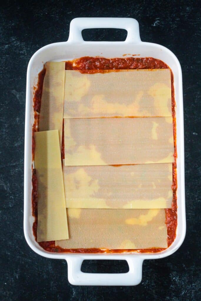 Lasagna noodles layered over sauce in a baking dish.