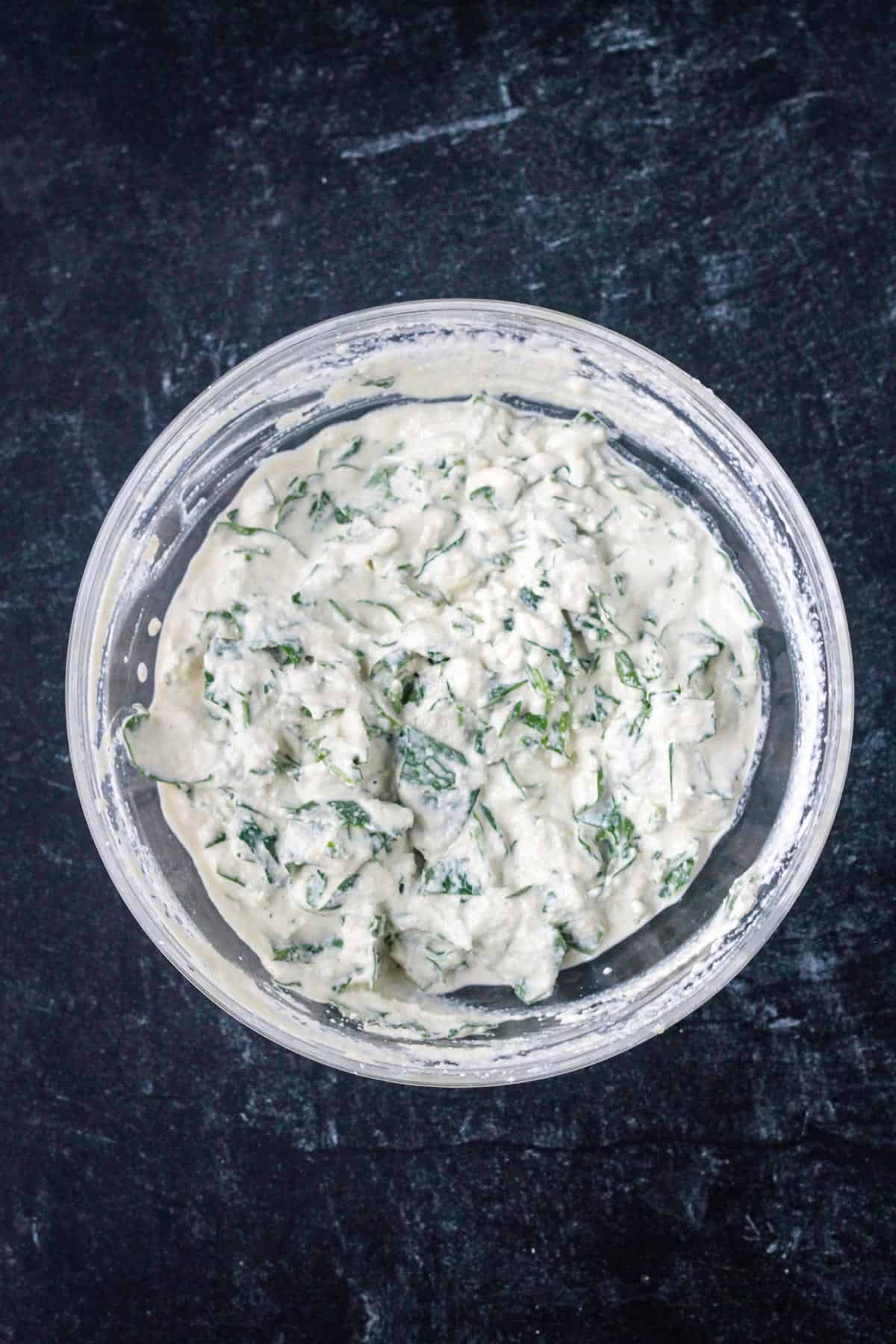 Vegan ricotta cheese mixed with fresh spinach in a bowl.