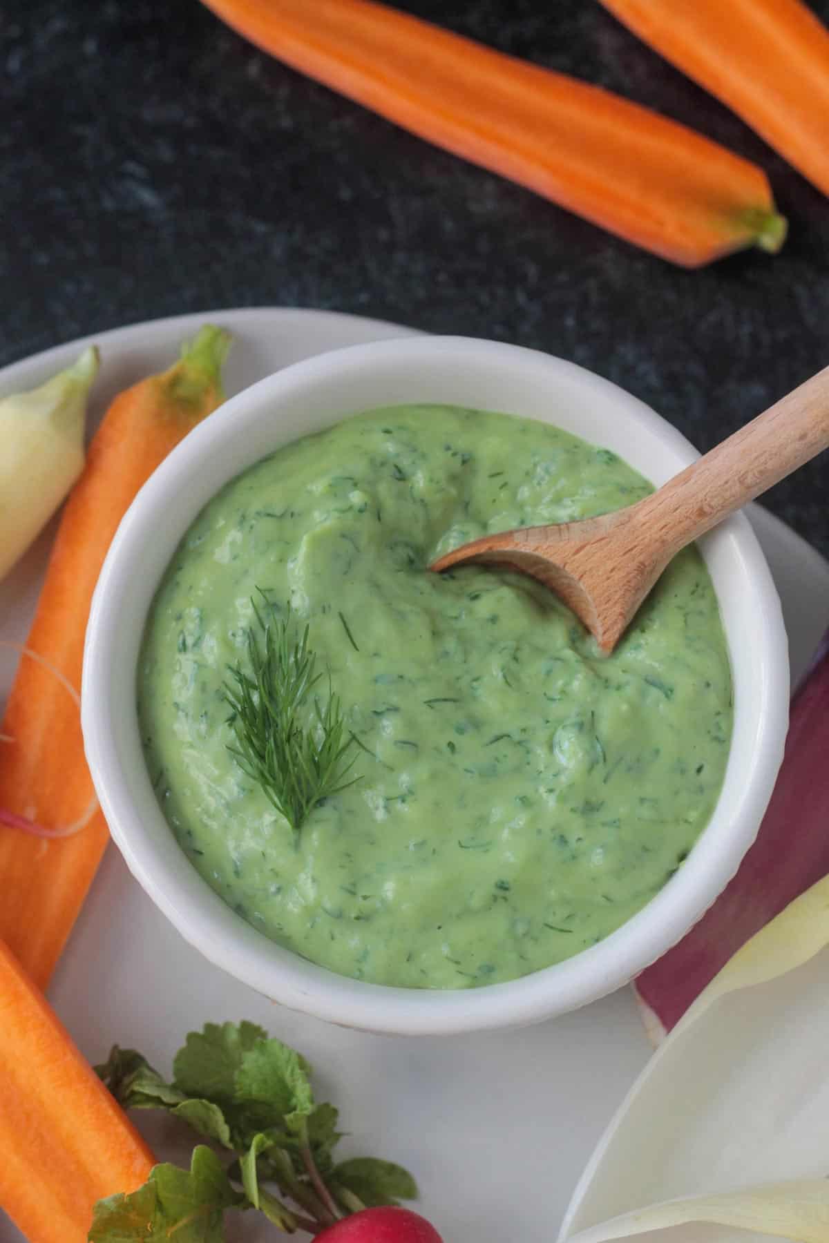 Close up of creamy green goddess dip in a white bowl.