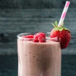 Dark pink smoothie in a glass with a pink and white striped straw.