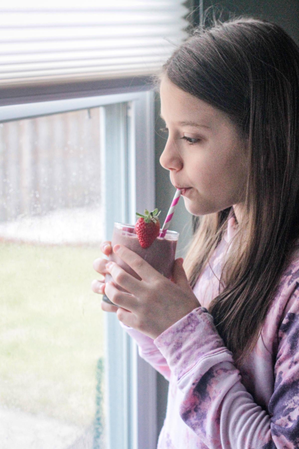 Young girl sipping a smoothie while looking out the window.