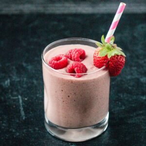 Chocolate mixed berry smoothie in a glass topped with three raspberries.