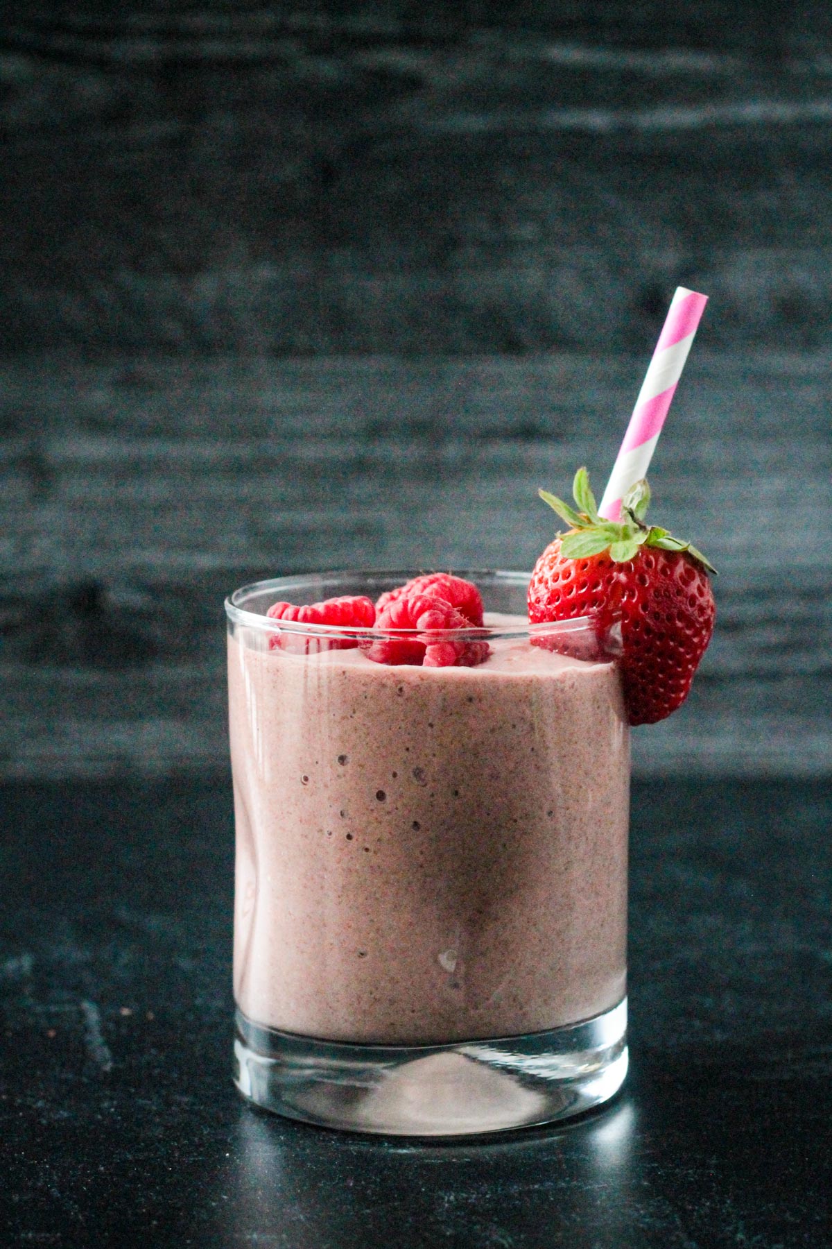 Dark pink berry smoothie in a glass with a pink and white striped straw.