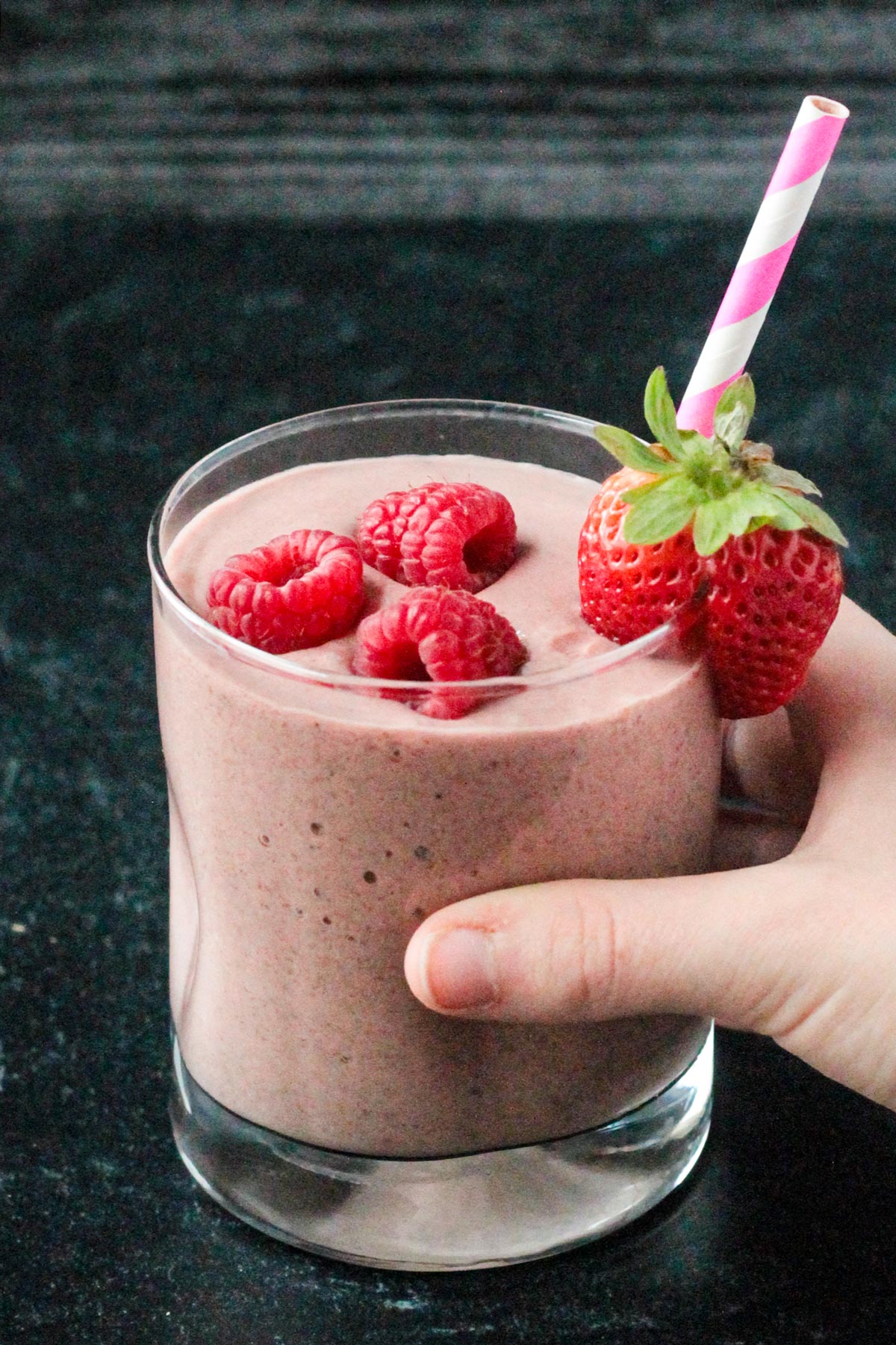 Hand reaching for a Chocolate Mixed Berry Smoothie in a glass.