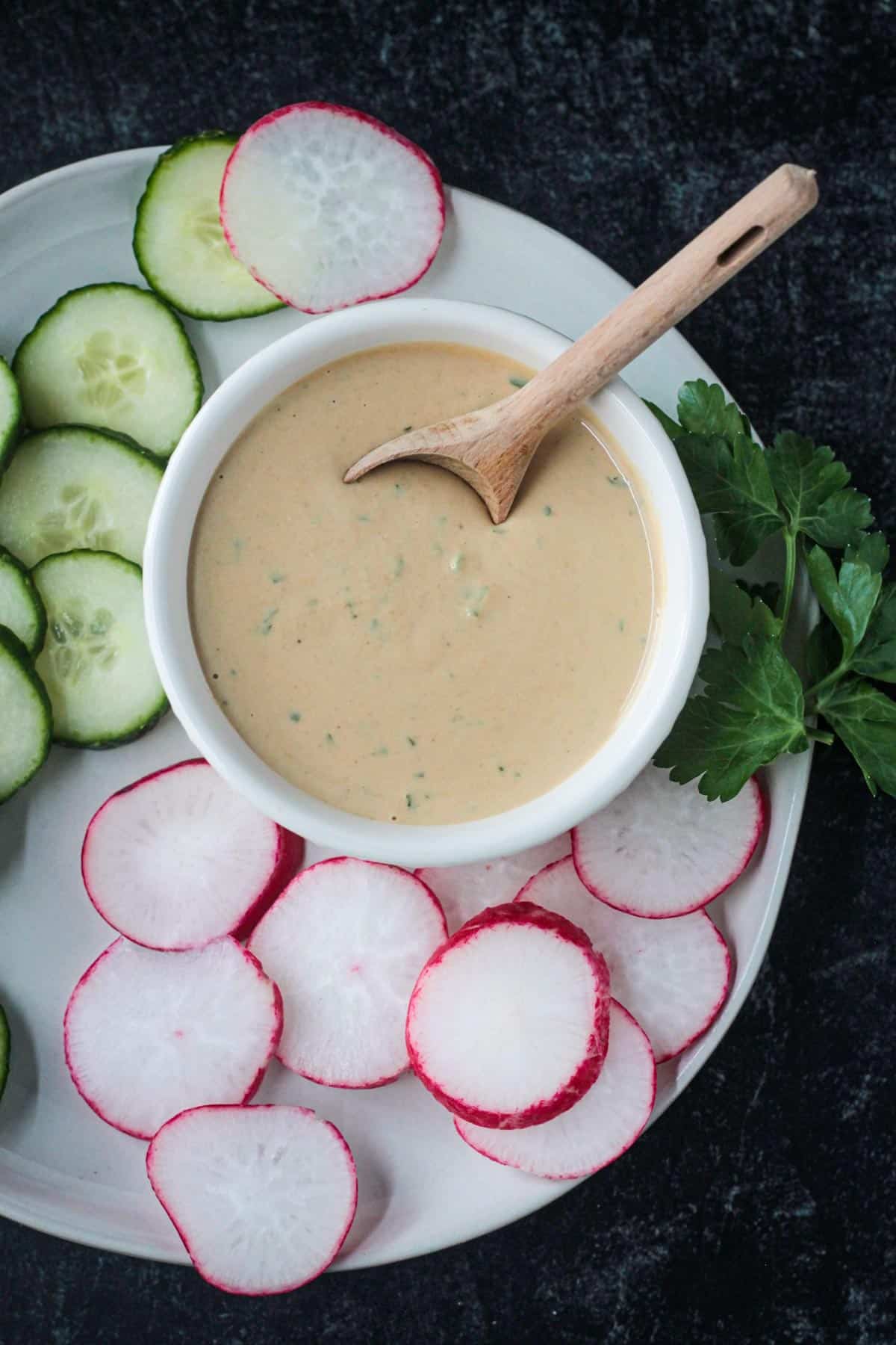 Close up of creamy goddess dressing in a bowl with a small wooden spoon.